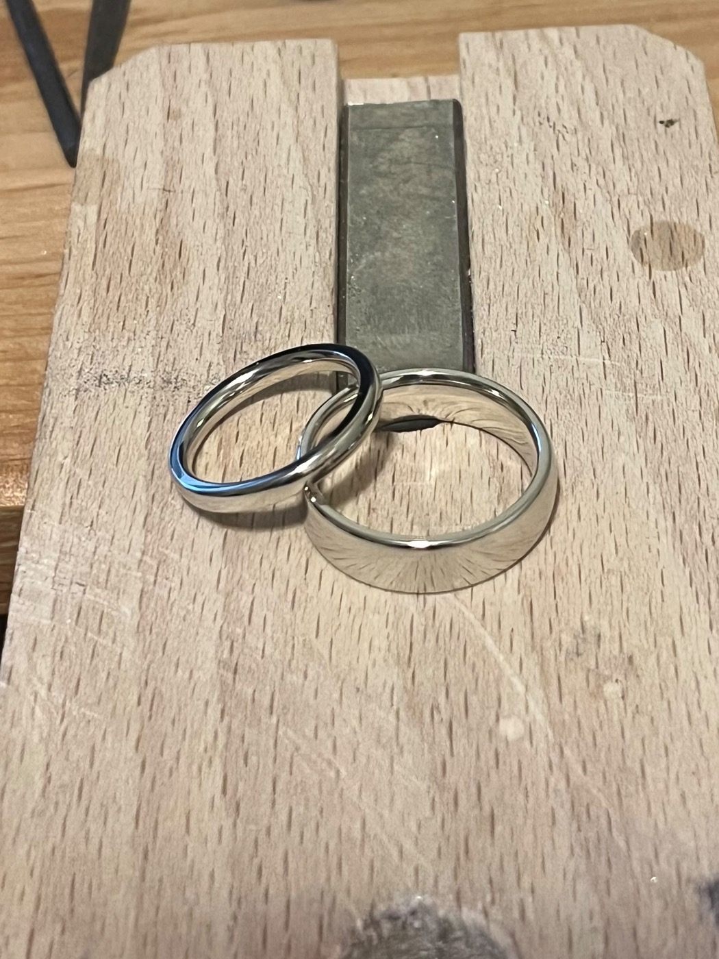 Two polished silver-coloured wedding bands resting on a wooden bench pin, with jeweller's files behind them.